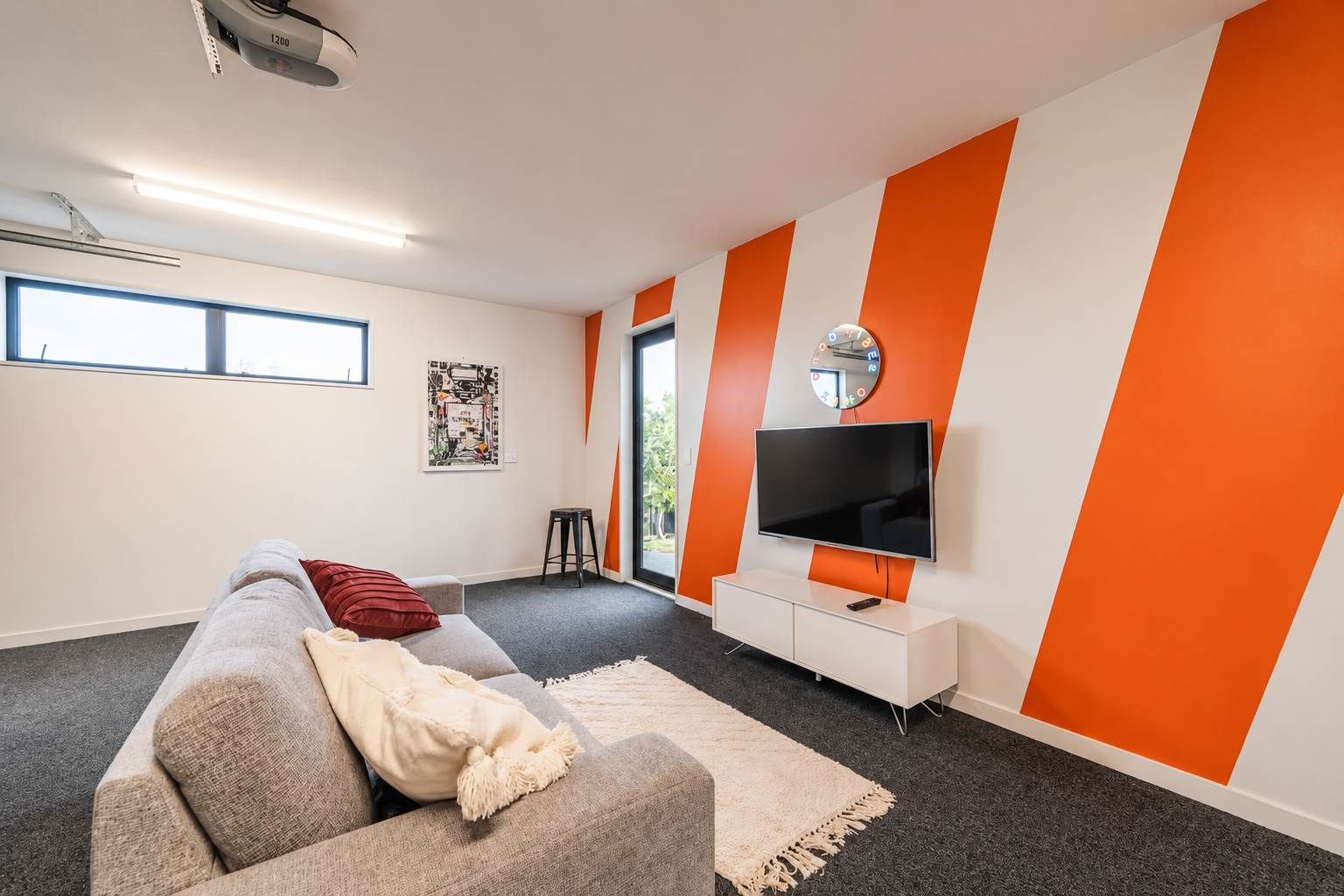 A modern living room with a grey sofa, a red pillow, a white throw blanket, a flat-screen TV, and a white entertainment unit.