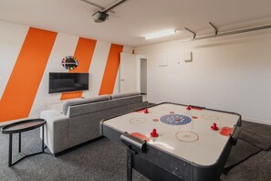 Una habitación con mesa de fútbol, sofá, televisor montado en la pared y diseño de pared a rayas.