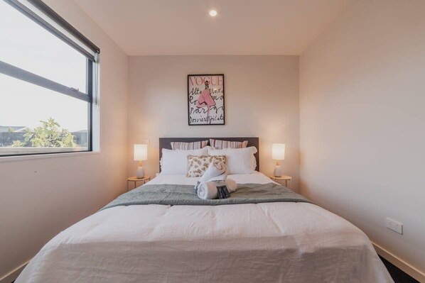 A neatly made bed with white linens and a green throw blanket, two bedside lamps, and a framed picture on the wall.