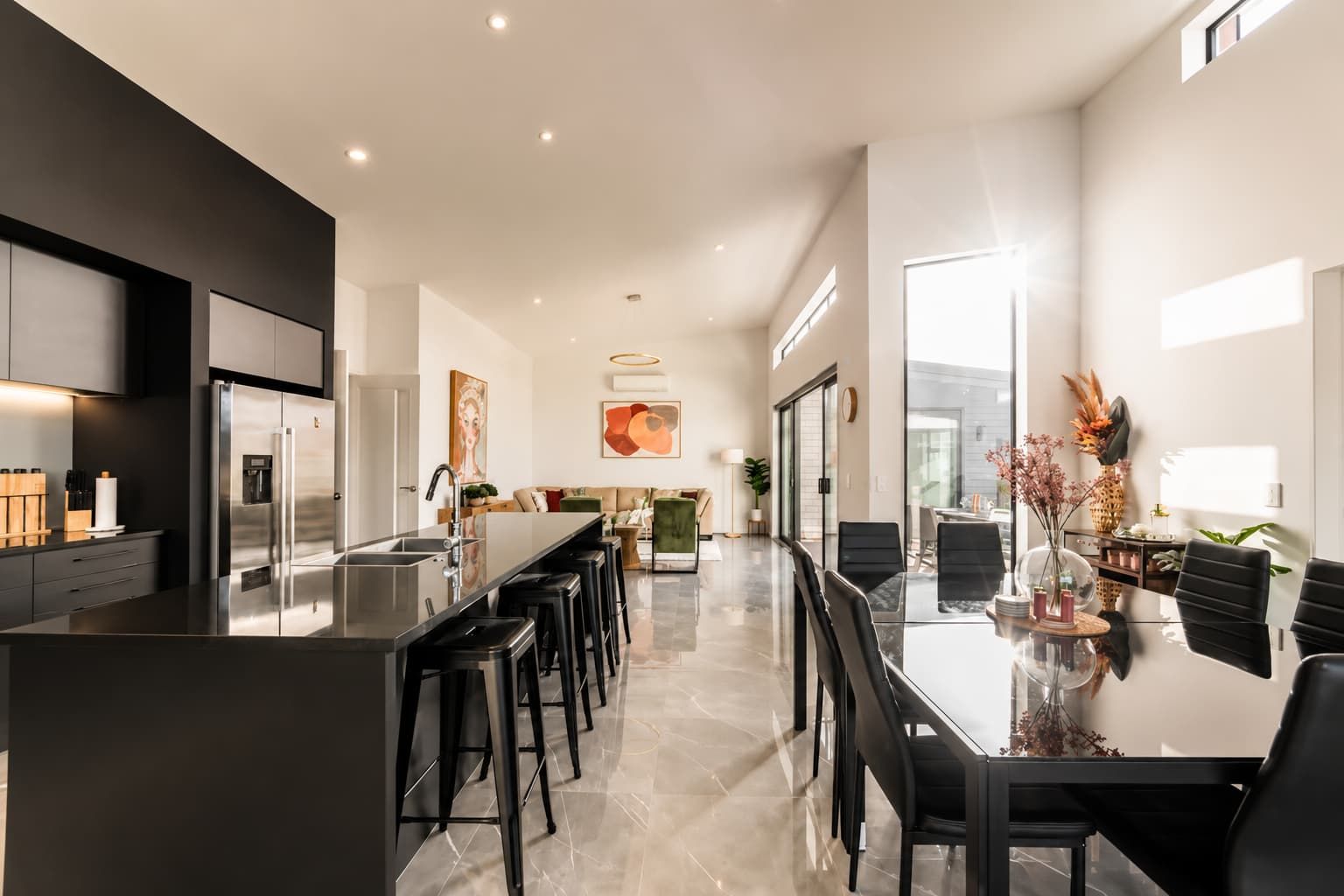 A modern kitchen with a central island, bar stools, and a dining area with a glass table and chairs.