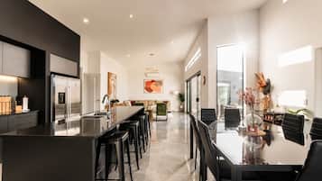 Una cucina moderna con isola centrale, sgabelli da bar e zona pranzo con tavolo in vetro e sedie.