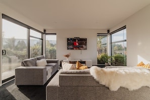 A modern living room with a grey sofa, a white fur throw, and a TV mounted on the wall. - Zenith Escapes Your Quintessential 4BR Haven (Christchurch)