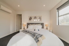 A modern hotel room with a large bed, two bedside lamps, a window with a view, and a door leading to another room. - Zenith Escapes Your Quintessential 4BR Haven (Christchurch)