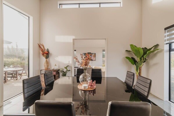 Un comedor moderno con una mesa de vidrio, sillas negras y un jarr ón con flores secas.
