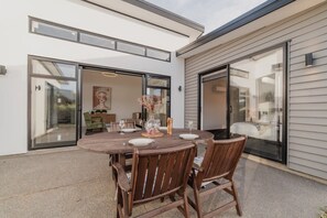 An outdoor patio with a round wooden table set for dining, surrounded by chairs.
