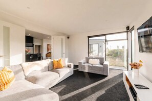 Una sala de estar moderna con un sofá gris, un sillón gris más pequeño y una mesa de centro. Se ve una ventana grande que ofrece vistas al exterior.