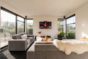 Un salon moderne avec un canapé gris, un plaid en fausse fourrure blanche et un téléviseur fixé au mur.