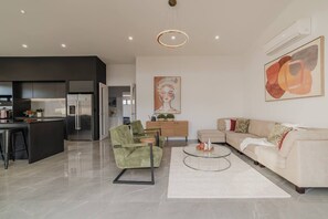 Un salon moderne avec un canapé, une table basse et un fauteuil vert. Il y a également un coin cuisine avec un réfrigérateur et une table à manger.