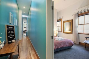 Une chambre d’hôtel avec un lit, un bureau et une chaise. Un couloir mène à la chambre, et un panneau est accroché au mur.