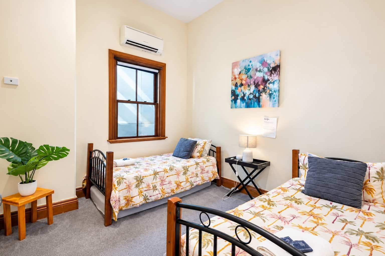 Une chambre avec deux lits simples, une fenêtre, un appareil de climatisation, un tableau et une lampe de chevet.