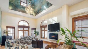 Un salon spacieux avec un haut plafond, un grand téléviseur et une cheminée.