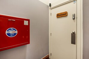 Un couloir avec un coffre rouge contenant un tuyau d’incendie et une porte portant l’inscription « Birdsnest ».