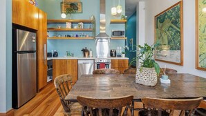 Une cuisine moderne avec des meubles en bois, un réfrigérateur en acier inoxydable, un four à micro-ondes et un évier. On y trouve une table à manger avec des chaises et une plante décorative.