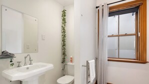 A bathroom with a white sink, toilet, and a window with a wooden frame and white curtains. - The Birds Nest - Central City Loft (Wellington)