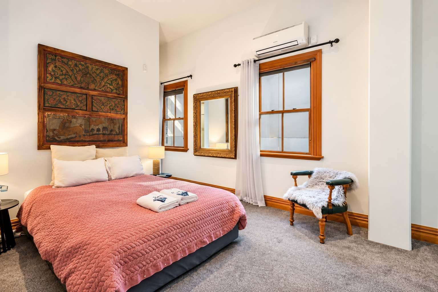 Une chambre d’hôtel avec un grand lit, une chaise, un miroir et des œuvres d’art accrochées aux murs.