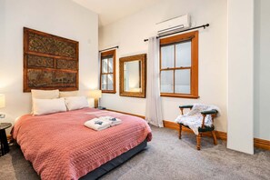 A hotel room with a large bed, a chair, a mirror, and artwork on the walls.