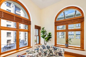 A room with two large arched windows, a sofa with floral upholstery, and a potted plant.
