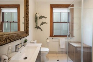 Une salle de bain moderne avec un grand miroir, deux fenêtres, une douche et des toilettes.