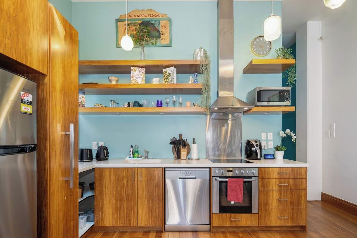 A modern kitchen with wooden cabinets, stainless steel appliances, and a teal backsplash.