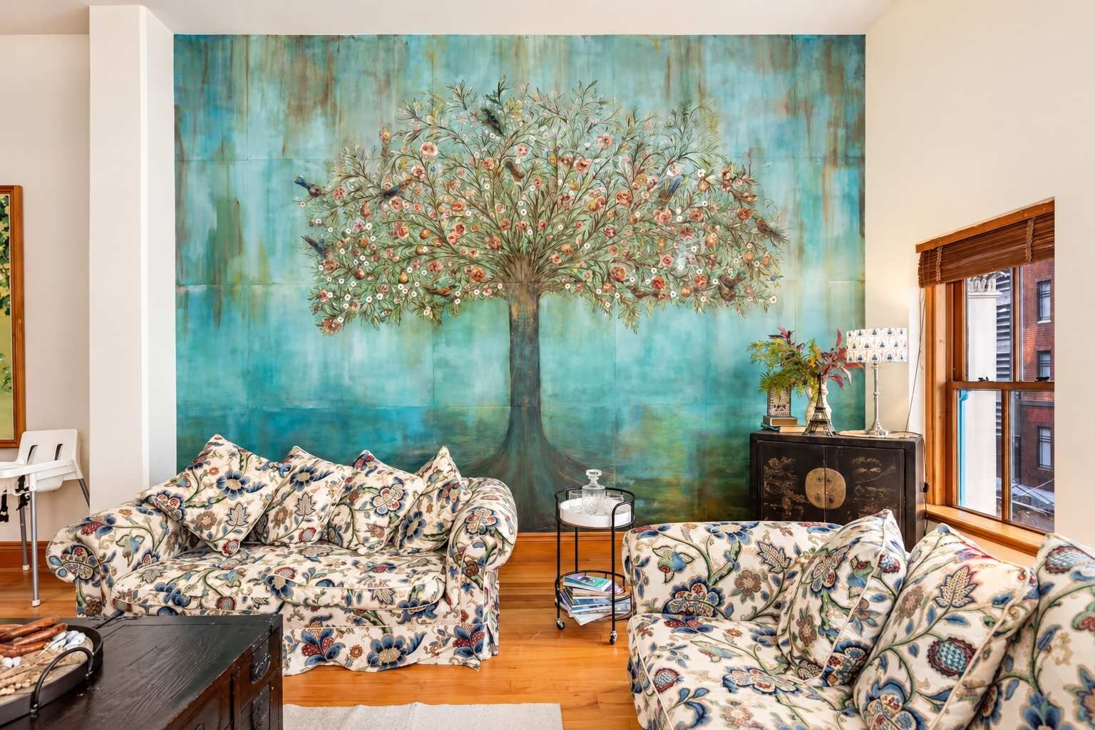 Una sala de estar con un gran mural floral, dos sofás estampados, una mesita auxiliar y un ventanal con vistas.