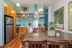 Une cuisine moderne avec des meubles en bois, un réfrigérateur en acier inoxydable, un four à micro-ondes et un évier. On y trouve une table à manger avec des chaises et une plante décorative.