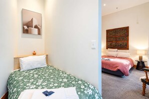 A hotel room with a single bed, a bedside table, a nightstand, a wall-mounted light, and a framed picture. - The Bird's Nest | 2BR Loft | Lambton Quay (Wellington)