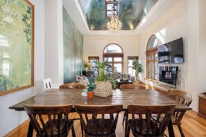 Un vaste espace dédié à la salle à manger, avec une grande table et des chaises en bois, entouré de canapés et de plantes en pot.