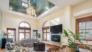 A spacious living room with a high ceiling, a large TV, and a fireplace. - The Birds Nest - Central City Loft (Wellington)