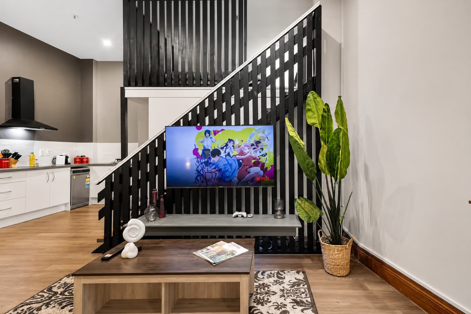 A modern living room with a TV, a coffee table, and a staircase with a black railing.