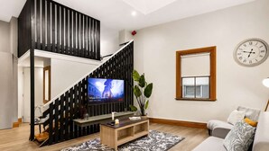 Una sala de estar moderna con una escalera, un televisor, un sofá y un reloj en la pared.