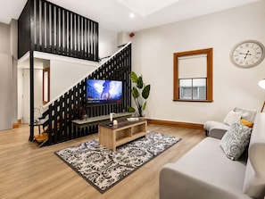 A modern living room with a staircase, a television, a sofa, and a clock on the wall.