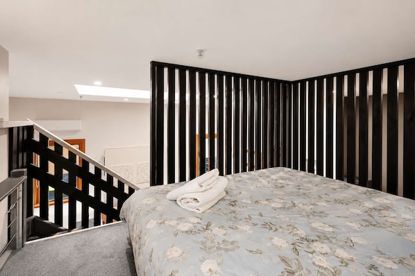 A bedroom with a bed, a staircase, and a view of a room with a wooden door.