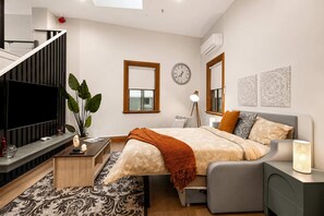 Quarto moderno com cama, mesa de cabeceira, abajur e televisão.