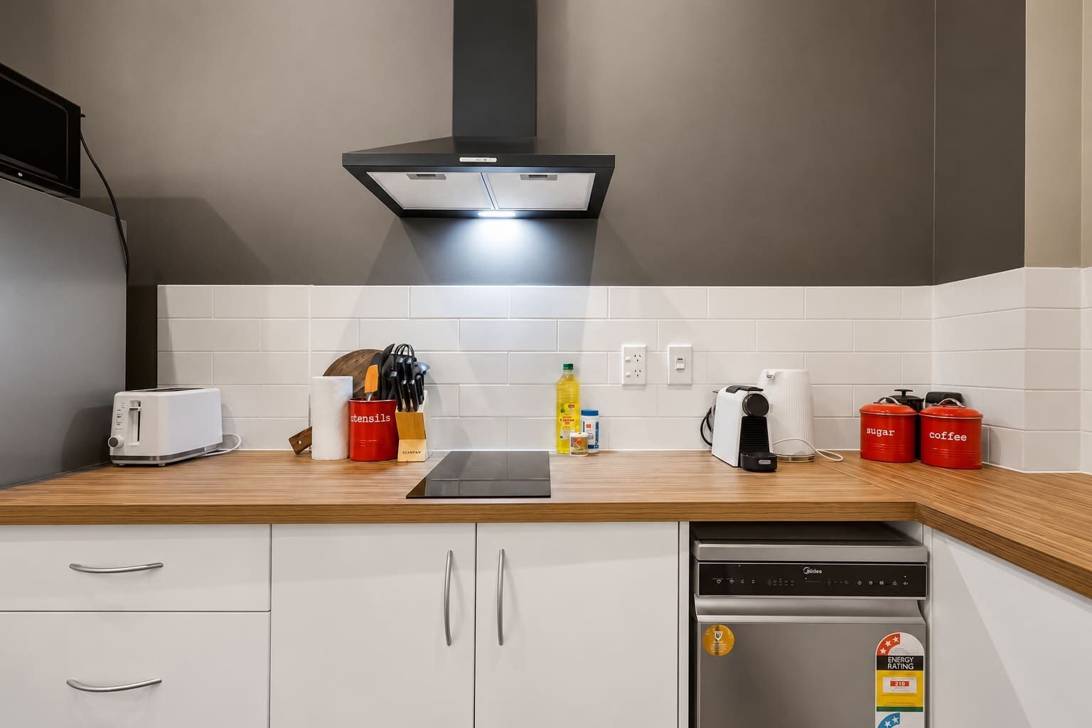 Una cocina moderna con un tostador, utensilios, una tetera y recipientes rojos etiquetados con azúcar y café.