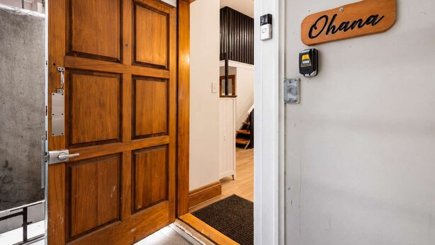 Una puerta de madera con un picaporte metálico, una placa con el nombre 'Ohana' y un dispositivo de seguridad en la pared.