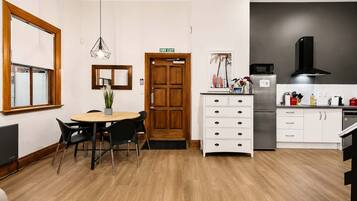 Una cocina compacta con comedor, una puerta de madera señalizada con 'FIRE EXIT', una lámpara colgante moderna y un refrigerador.