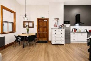 A compact kitchen with a dining area, a wooden door marked 'FIRE EXIT', a modern pendant light, and a refrigerator. - Wellington City Loft | Parking + Kitchen (Wellington)
