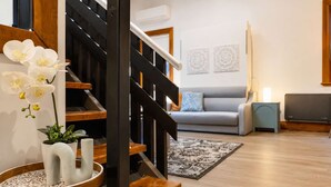 Una sala de estar moderna con una escalera, un sofá gris, una mesita con una planta y un televisor de pantalla plana.