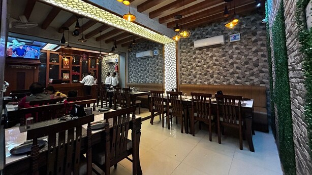 A restaurant interior with wooden ceiling beams, stone walls, and hanging pendant lights. Tables and chairs are arranged for dining. - The Heritage (Dumka)