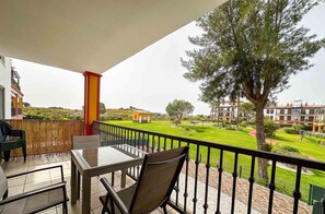Un balcón con mesa y sillas, con vistas a un jardín cuidado y edificios residenciales.