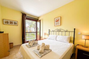Habitación de hotel con cama, mesita de noche, aparador de madera, ventana con vistas al exterior y puerta.