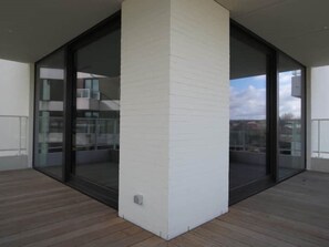 Um apartamento moderno com uma grande porta de vidro que dá para uma varanda, paredes de tijolo branco e piso de madeira.