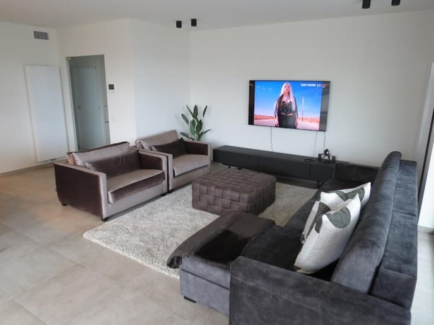 Ein modernes Wohnzimmer mit einem Ecksofa, einem Zweisitzer und einem Couchtisch. Ein Flachbildfernseher ist an der Wand befestigt.