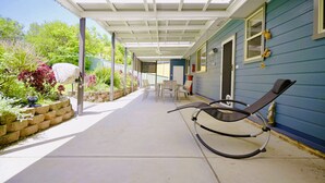 A covered patio with a chair, a table, and chairs, and a garden area with plants and a water feature.