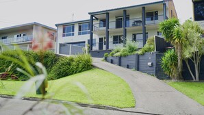 A modern two-story residential building with balconies, a well-maintained lawn, and a gated driveway.