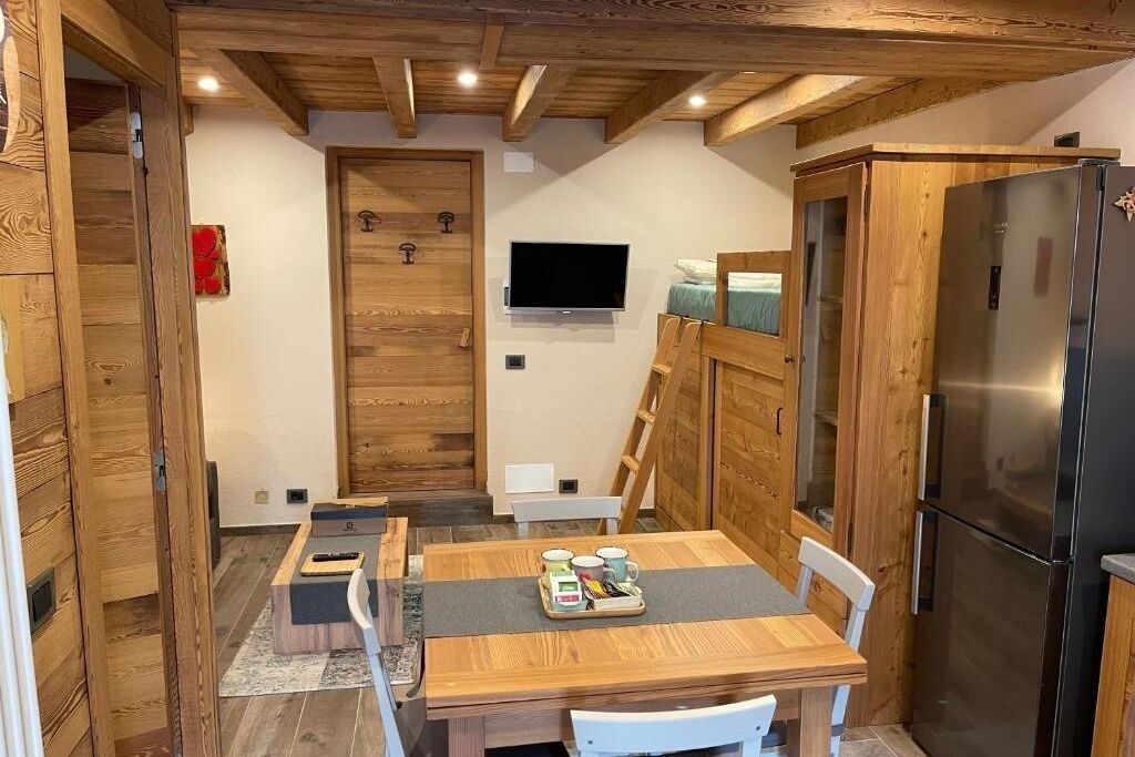 Eine kompakte Küche mit Holzschränken, einem Edelstahlkühlschrank, einem Esstisch mit Stühlen und einem an der Wand befestigten Fernseher.