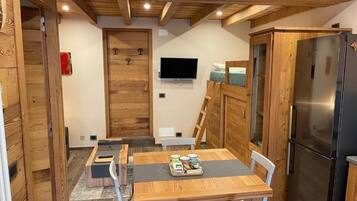 Eine kompakte Küche mit Holzschränken, einem Edelstahlkühlschrank, einem Esstisch mit Stühlen und einem an der Wand befestigten Fernseher.