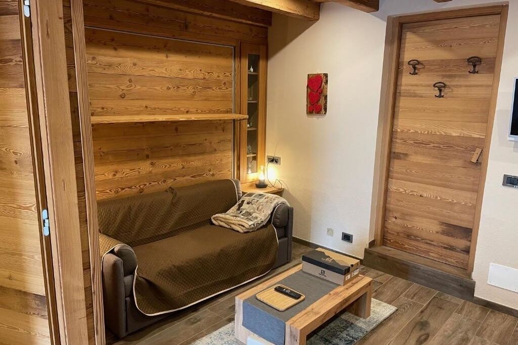 Un salon chaleureux avec un mur en bois, un canapé marron, une table basse et une porte en bois dotée d’une poignée.