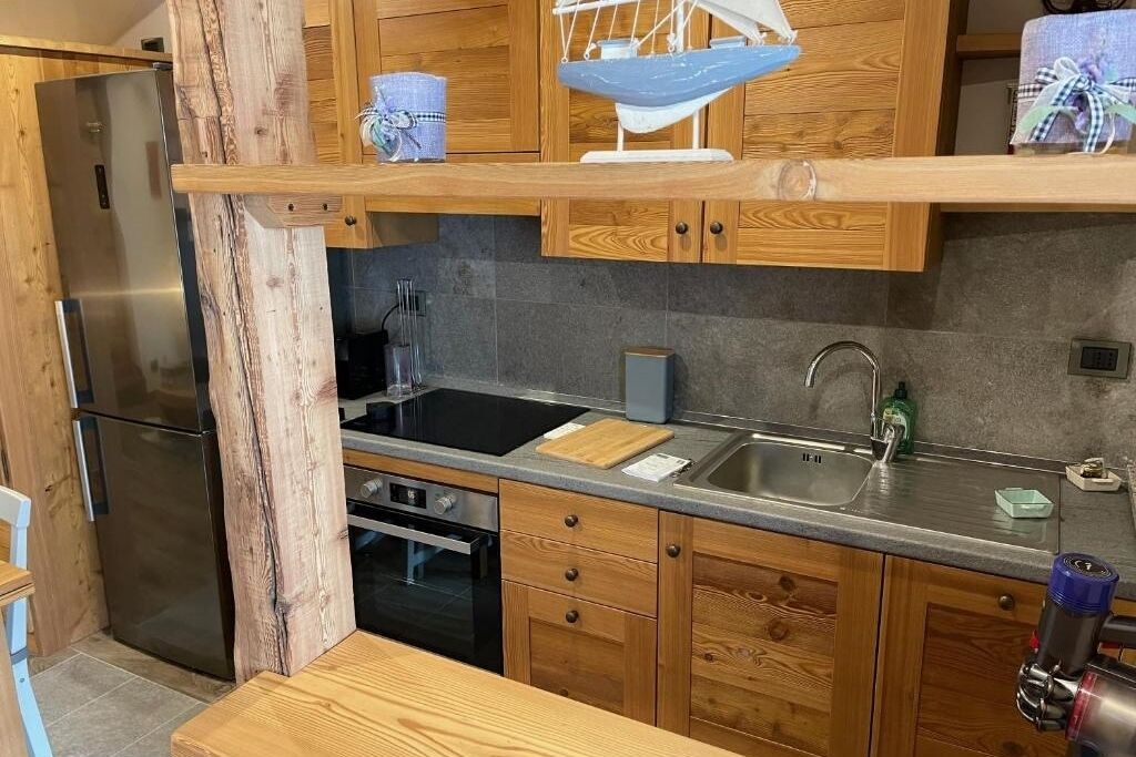 Eine Küche mit Holzausstattung, einem Edelstahlkühlschrank, einem schwarzen Herd und einem Spülbecken.