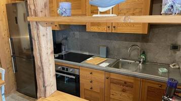 Eine Küche mit Holzausstattung, einem Edelstahlkühlschrank, einem schwarzen Herd und einem Spülbecken.